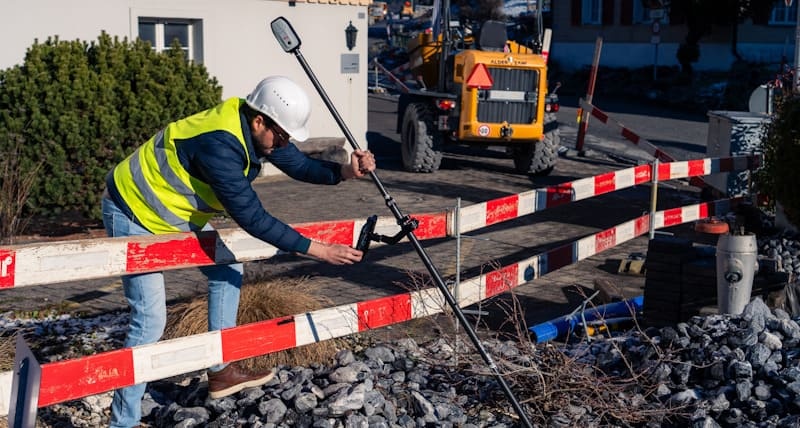 Geometre avec casque et gilet reflechissant mesurant avec Leica Zeno FLX100 Plus Tilt sur chantier routier