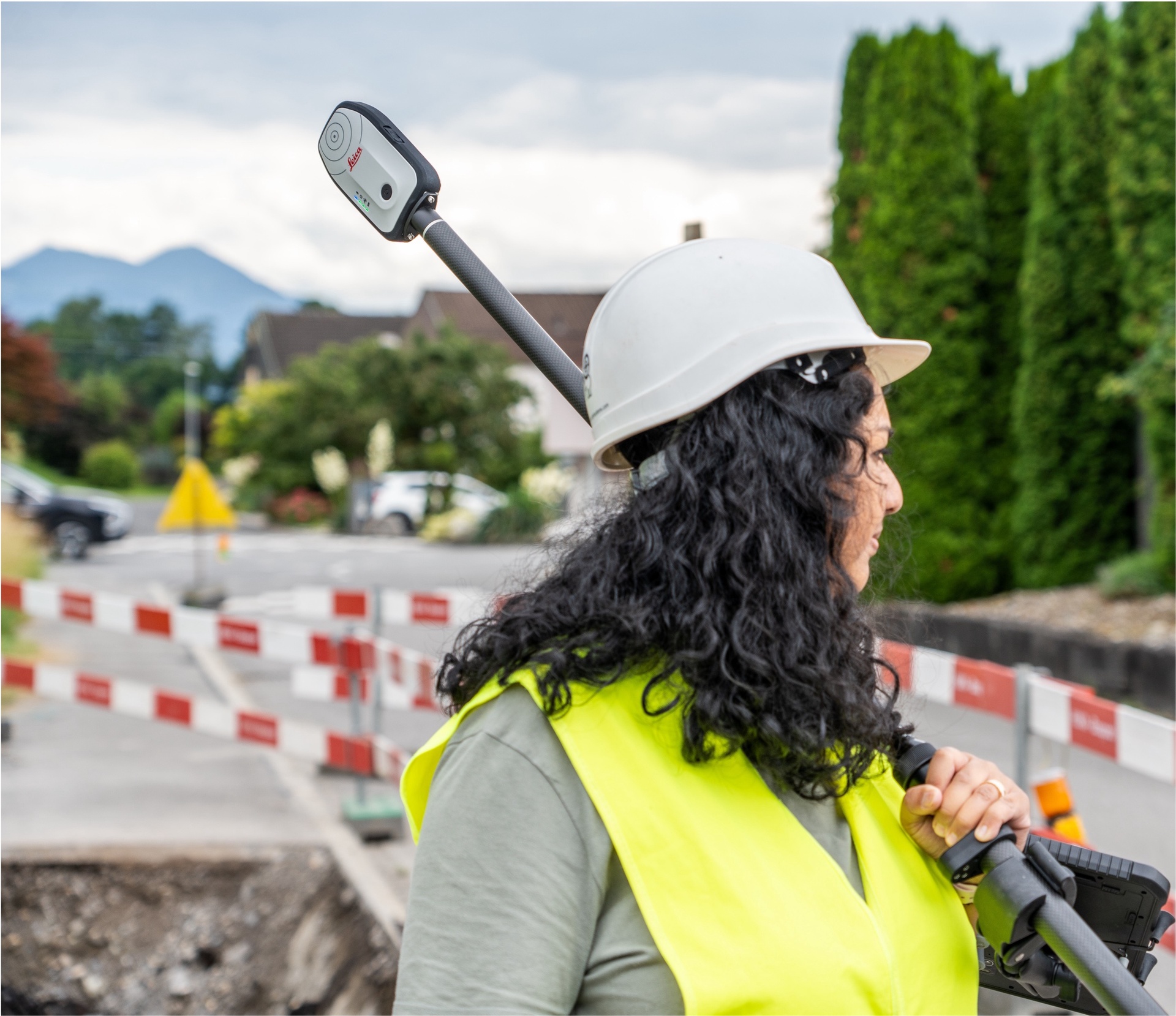 Geometre avec casque et Leica Zeno FLX100 Plus Tilt sur mire dans la rue avec montagnes en arriere-plan