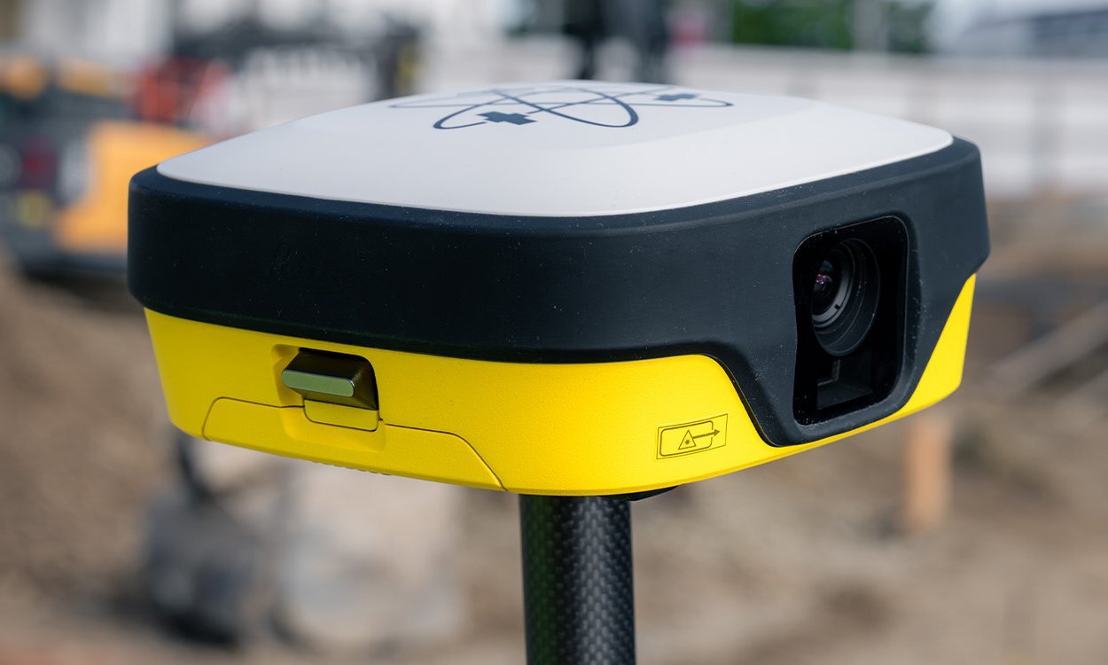 Antenne intelligente GNSS Leica iCON iCG11 sur une canne, gros plan sur la caméra frontale, avec un chantier en arrière-plan